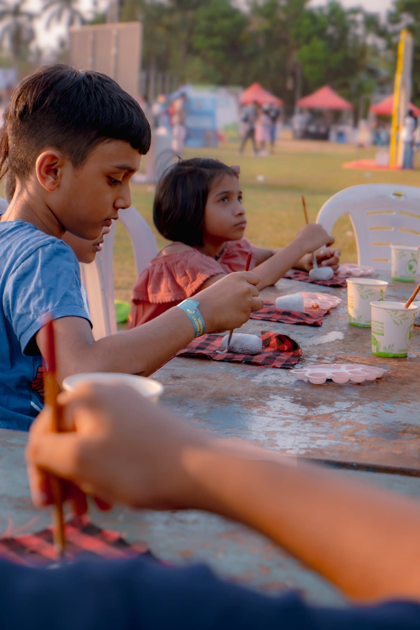 Children painting small stones together at an outdoor table.
