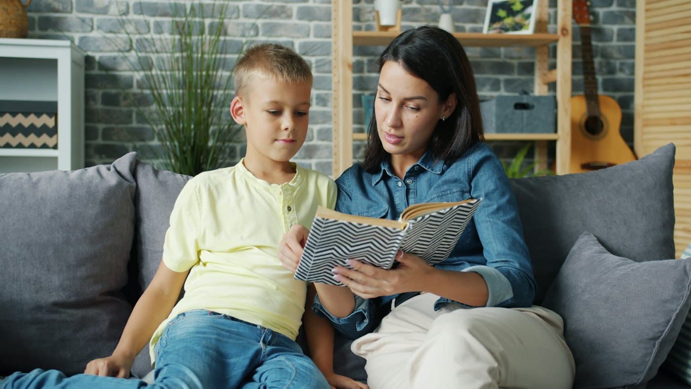 A parent and child sitting close on a sofa, looking at an open book together.