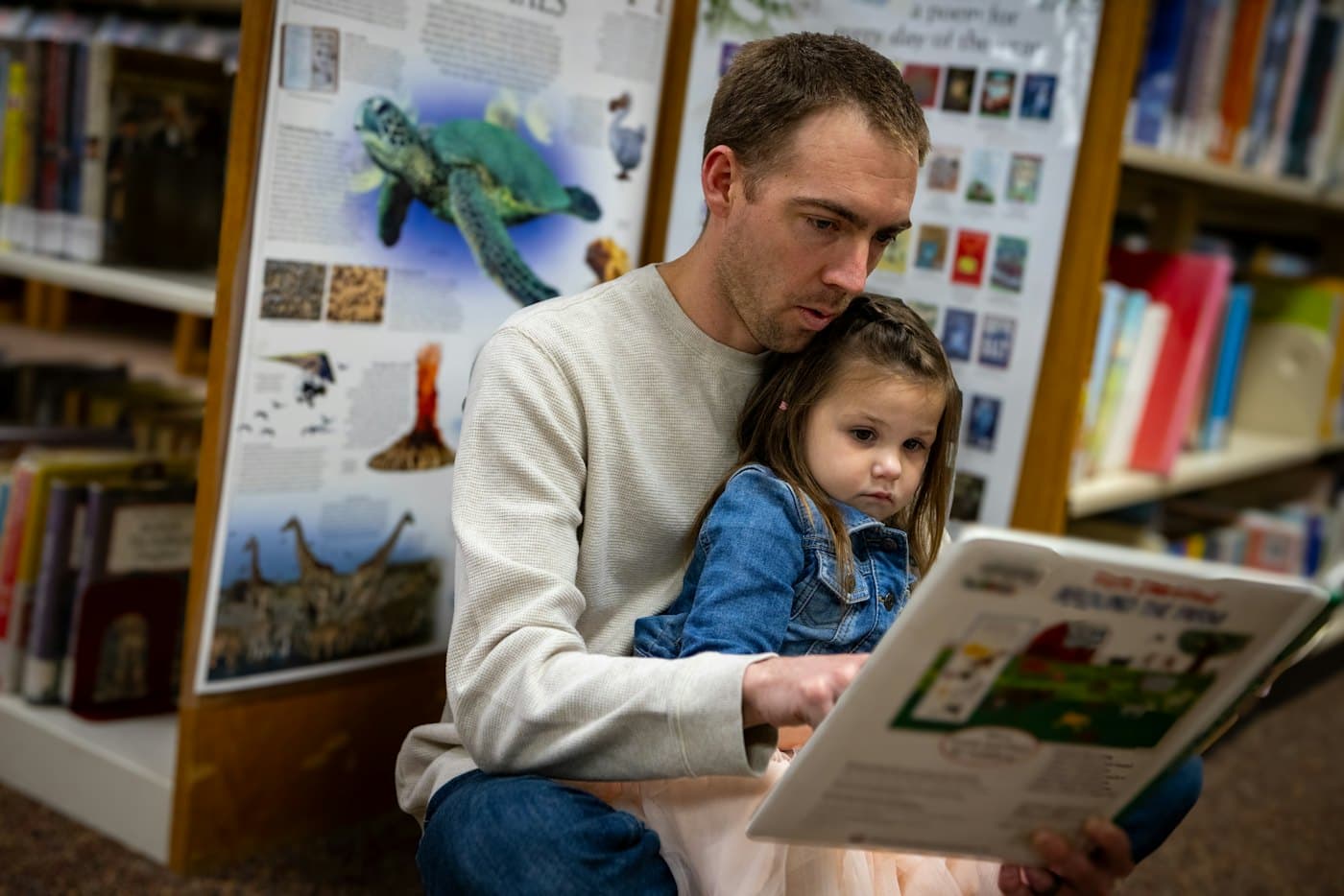 A father and a young child looking at a picture book in a library.